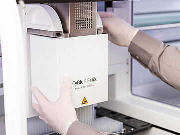 gloved hands changing the pipetting head on a CyBio Felix liquid handler