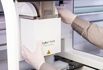 gloved hands changing the pipetting head on a CyBio Felix liquid handler
