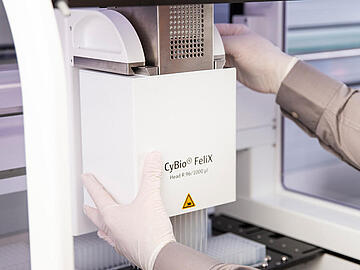 gloved hands changing the pipetting head on a CyBio Felix liquid handler