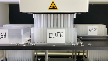 A CyBio Felix liquid handling robot pipetting into a deep well plate on the upper deck. A wash buffer reservoir is at left and a deep well 96-well wash plate is at right.