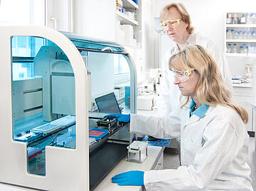 two people placing labware on the deck of a Felix liquid handler
