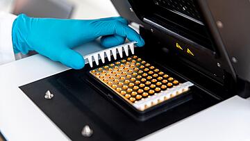 a gloved hand placing an 8-well PCR strip into the heating block of a qTOWER iris qPCR instrument