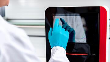 a gloved hand operating the touchscreen on a qTOWER iris Touch qPCR instrument